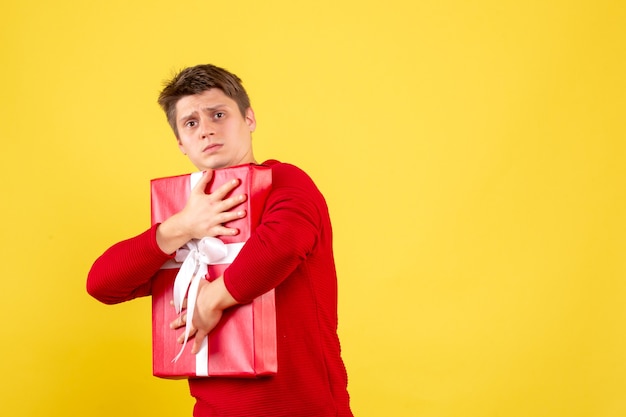 Front view of young man holding christmas present on yellow wall