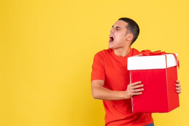 Front view of young man holding christmas present on yellow wall