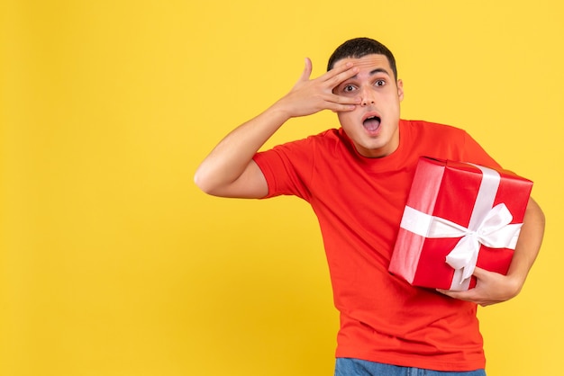 Front view of young man holding christmas present on yellow wall