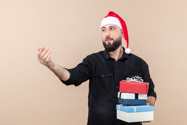 Front view of young man holding christmas presents on a pink wall