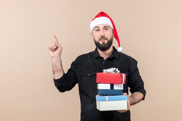 Front view of young man holding christmas presents on pink wall