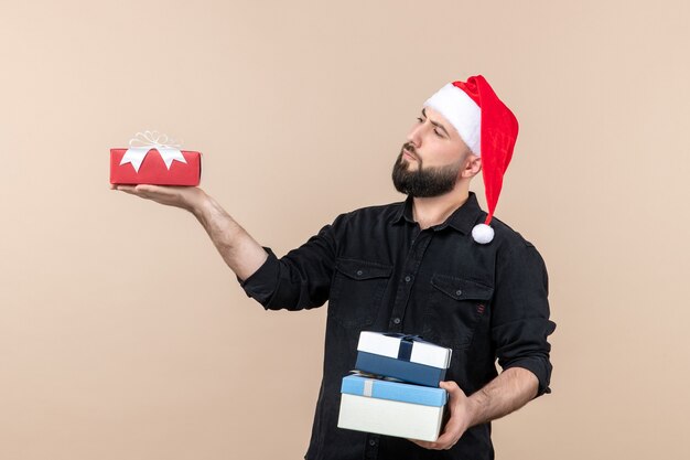 Front view of young man holding christmas presents on the pink wall