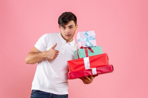 Front view of young man holding christmas presents on pink wall