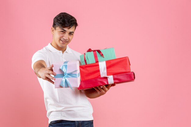 Front view of young man holding christmas presents on pink wall