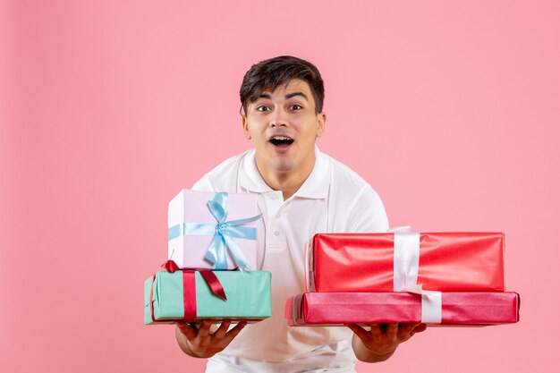 Front view of young man holding christmas presents on pink wall