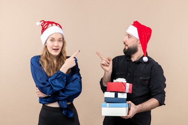 Front view of young man holding christmas presents with woman on pink wall