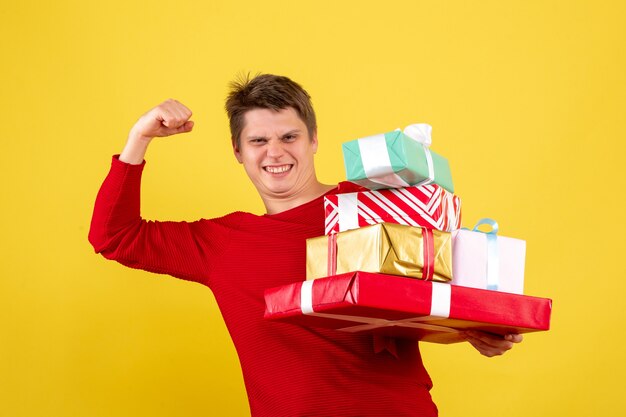 Front view of young man holding christmas presents on yellow wall