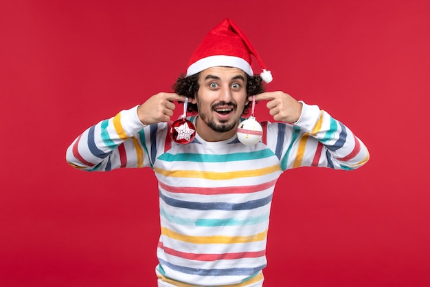 Front view young man holding christmas tree toys on red wall new year red holiday male