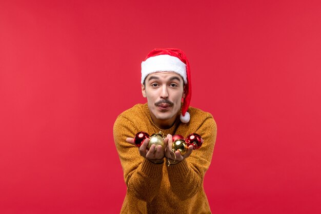 Front view of young man holding christmas tree toys on red wall