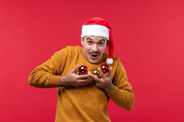 赤い壁にクリスマスツリーのおもちゃを保持している若い男の正面図