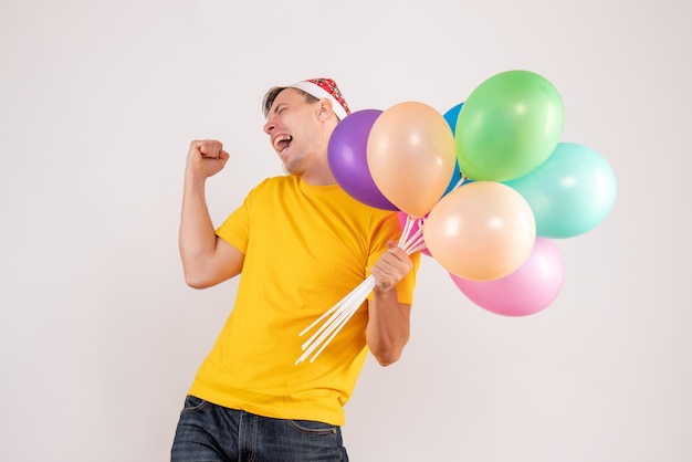 Front view of young man holding colorful balloons on a white wall