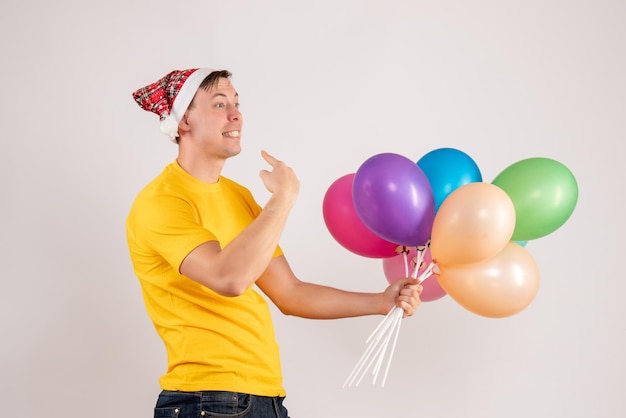 Front view of young man holding colorful balloons on a white wall