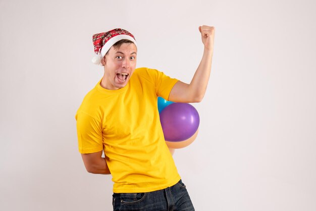 Front view of young man holding colorful balloons on a white wall