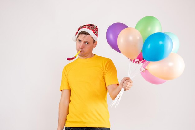 Front view of young man holding colorful balloons on a white wall