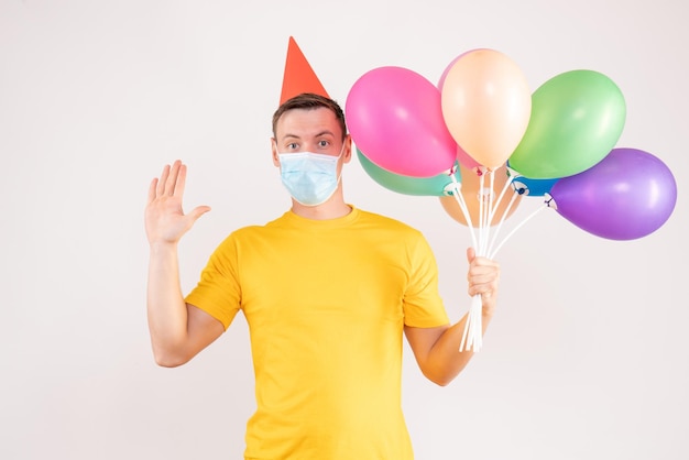 Front view of young man holding colorful balloons on a white wall