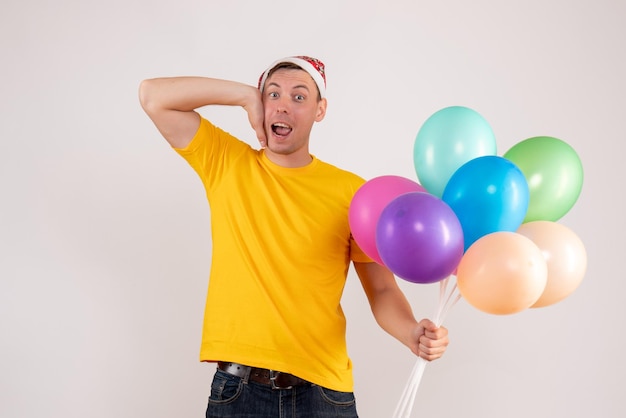 Front view of young man holding colorful balloons on a white wall