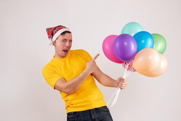 Front view of young man holding colorful balloons on a white wall