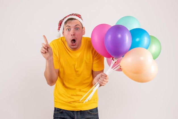 Front view of young man holding colorful balloons on a white wall