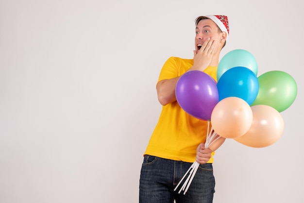 Front view of young man holding colorful balloons on a white wall