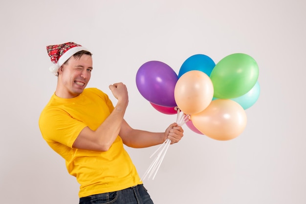 Front view of young man holding colorful balloons on the white wall