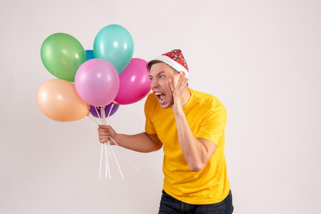 Front view of young man holding colorful balloons on the white wall