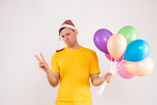 Front view of young man holding colorful balloons on the white wall