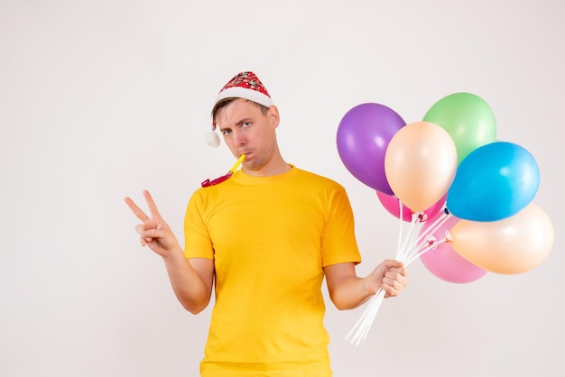 Front view of young man holding colorful balloons on the white wall