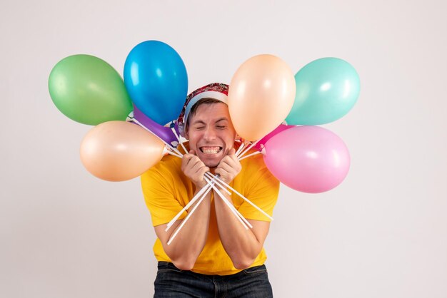 Front view of young man holding colorful balloons on the white wall