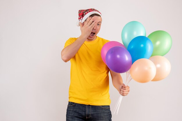 Front view of young man holding colorful balloons on the white wall