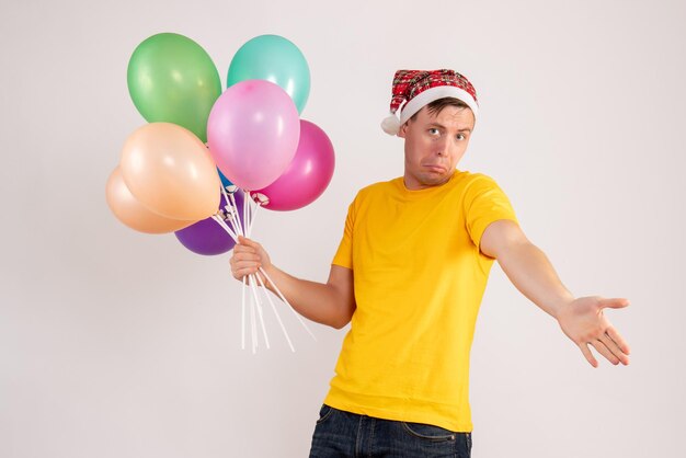 Front view of young man holding colorful balloons on white wall