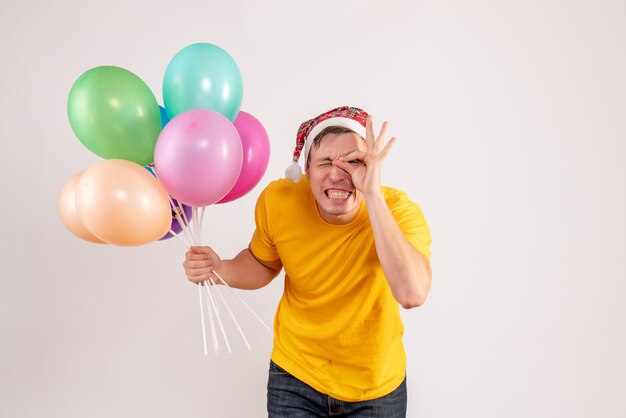 白い壁にカラフルな風船を保持している若い男の正面図