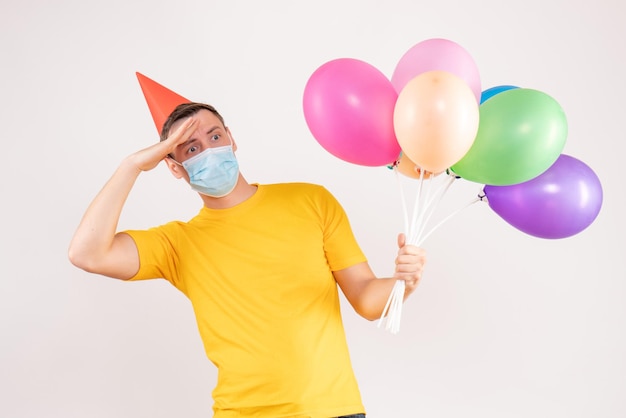 白い壁にカラフルな風船を保持している若い男の正面図