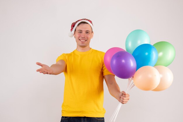 Front view of young man holding colorful balloons on white wall