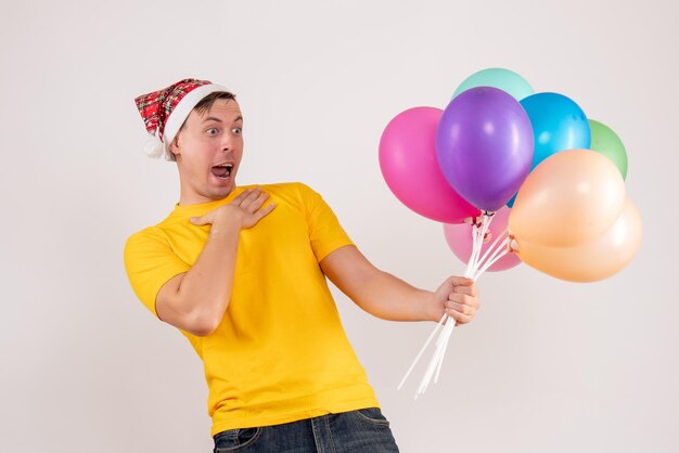 Front view of young man holding colorful balloons on white wall