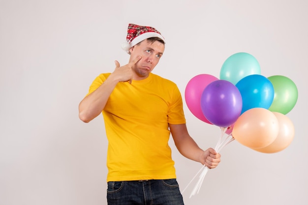 Front view of young man holding colorful balloons on white wall
