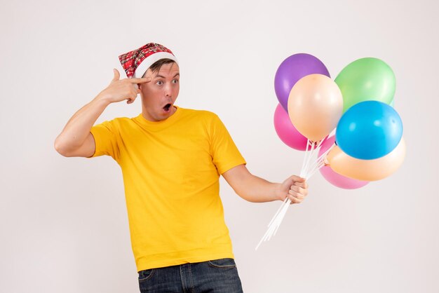 Front view of young man holding colorful balloons on white wall