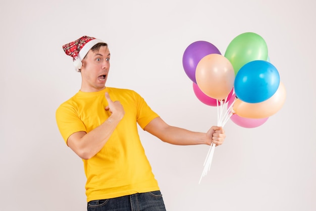 front view of young man holding colorful balloons on white wall