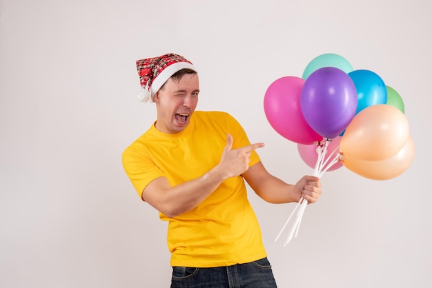 front view of young man holding colorful balloons on white wall
