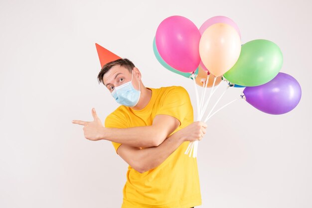 Front view of young man holding colorful balloons on white wall