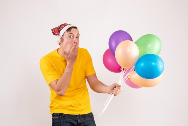 Front view of young man holding colorful balloons on a white wall