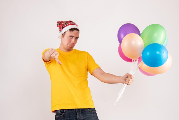 흰 벽에 다채로운 풍선을 들고 있는 젊은 남자의 전면 모습