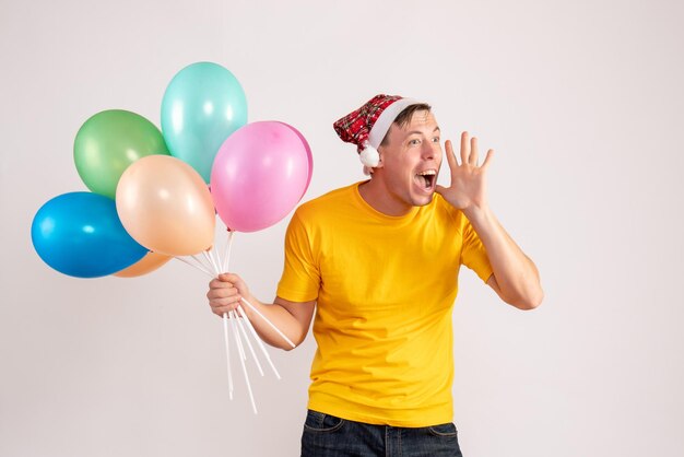 Front view of young man holding colorful balloons on white wall