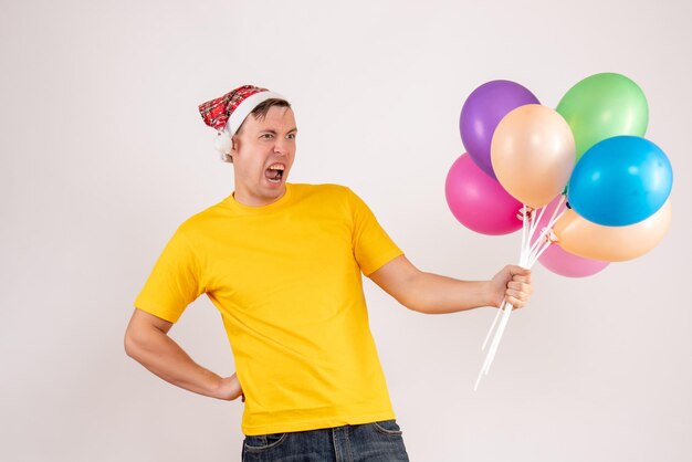 Front view of young man holding colorful balloons on white wall