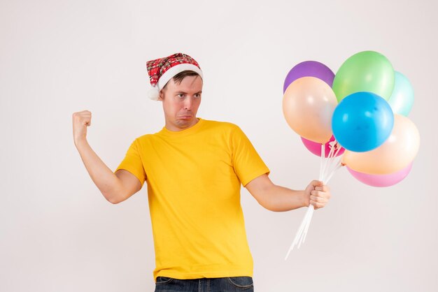 Вид спереди молодого человека, держащего разноцветные шары на белой стене