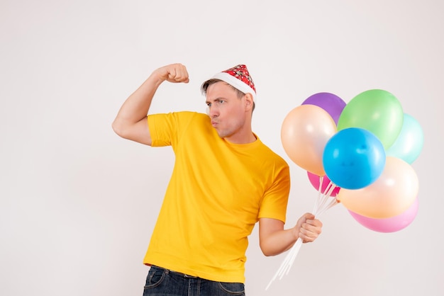 Front view of young man holding colorful balloons on white wall