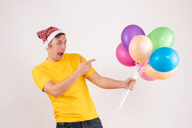 Front view of young man holding colorful balloons on white wall