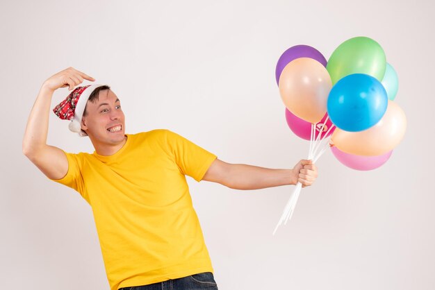 Front view of young man holding colorful balloons on white wall