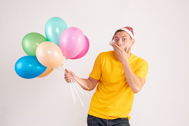 Front view of young man holding colorful balloons on white wall