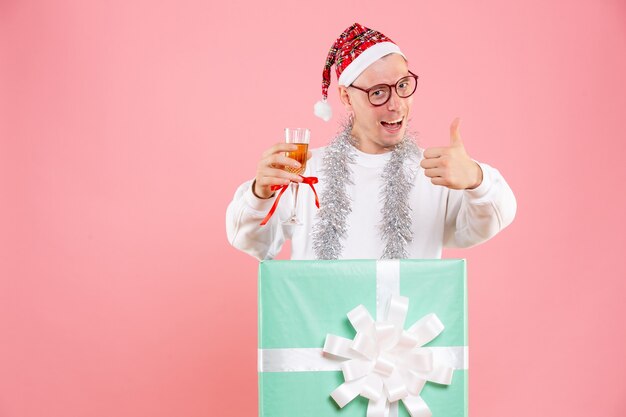 Вид спереди молодого человека, держащего напиток с гирляндами в рождественском настроении на розовой стене