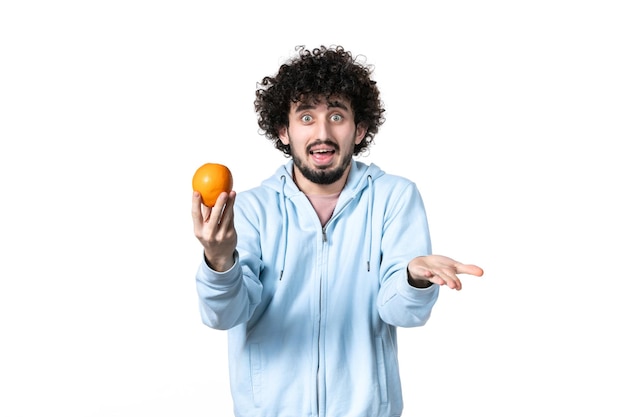 Бесплатное фото Вид спереди молодой человек, держащий свежий апельсин на белом фоне, похудение, похудение, измерение человеческого тела